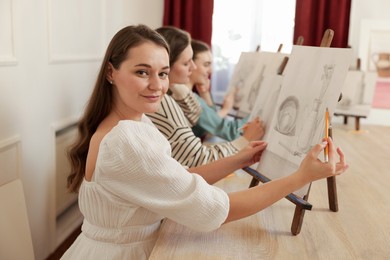 Group of women with easels learning to draw at wooden table in class