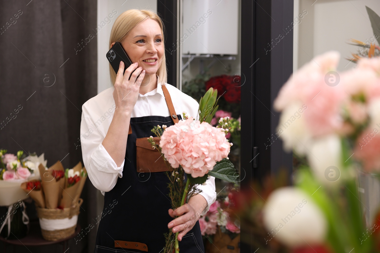 Photo of Business owner with beautiful bouquet talking on smartphone in her flower shop