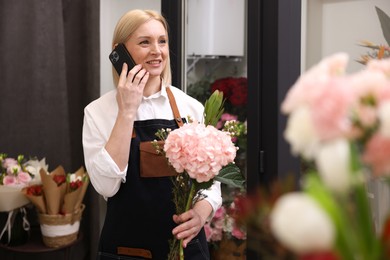 Business owner with beautiful bouquet talking on smartphone in her flower shop