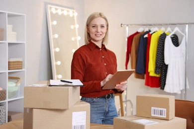 Photo of Business owner using tablet near table with parcels in her tailor shop