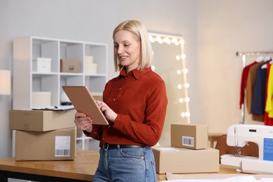 Photo of Business owner using tablet near table with parcels in her tailor shop