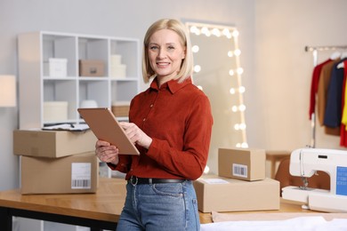 Business owner using tablet near table with parcels in her tailor shop