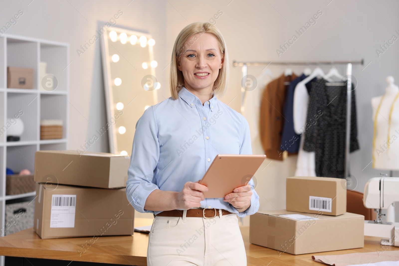 Photo of Business owner using tablet near table with parcels in her tailor shop