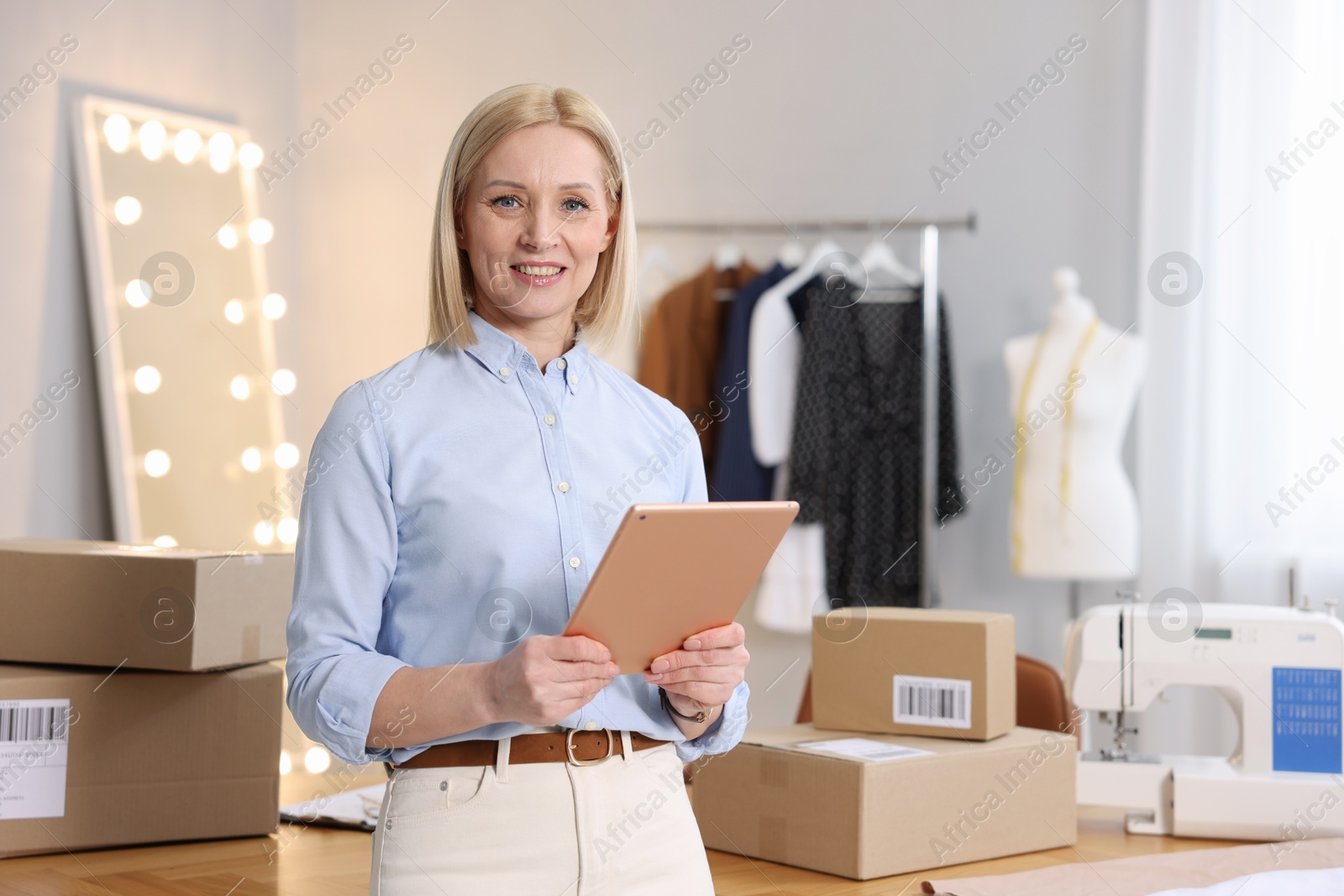 Photo of Business owner using tablet near table with parcels in her tailor shop