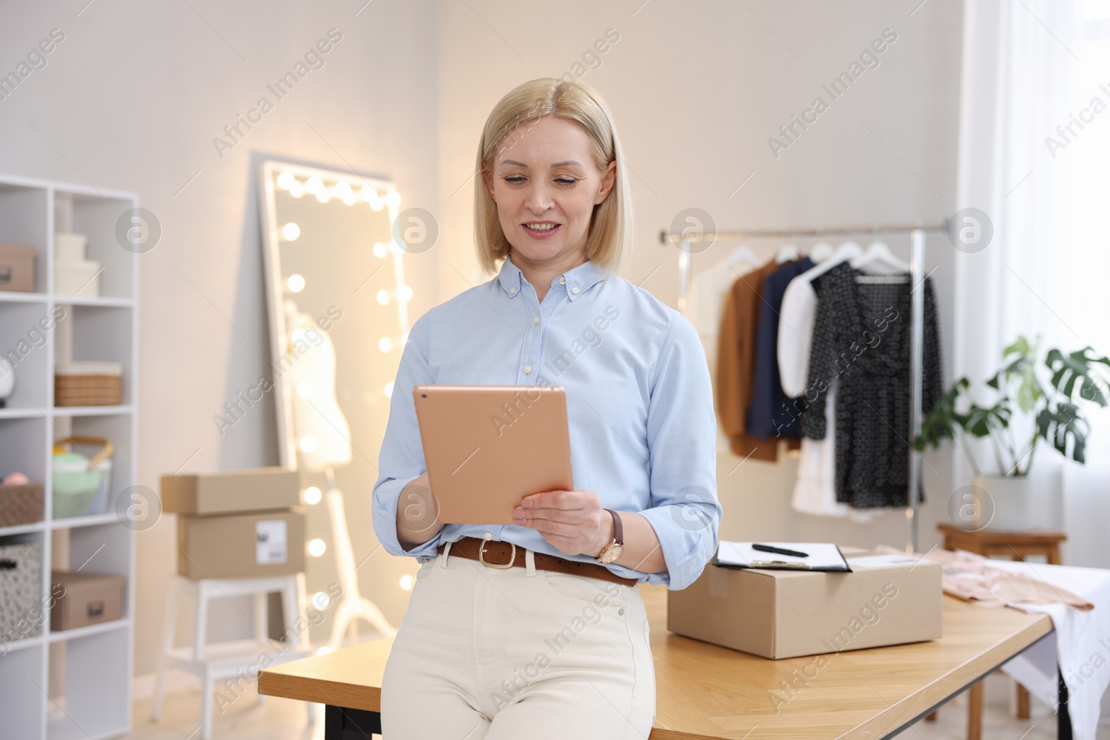 Photo of Business owner using tablet near table with parcel in her tailor shop