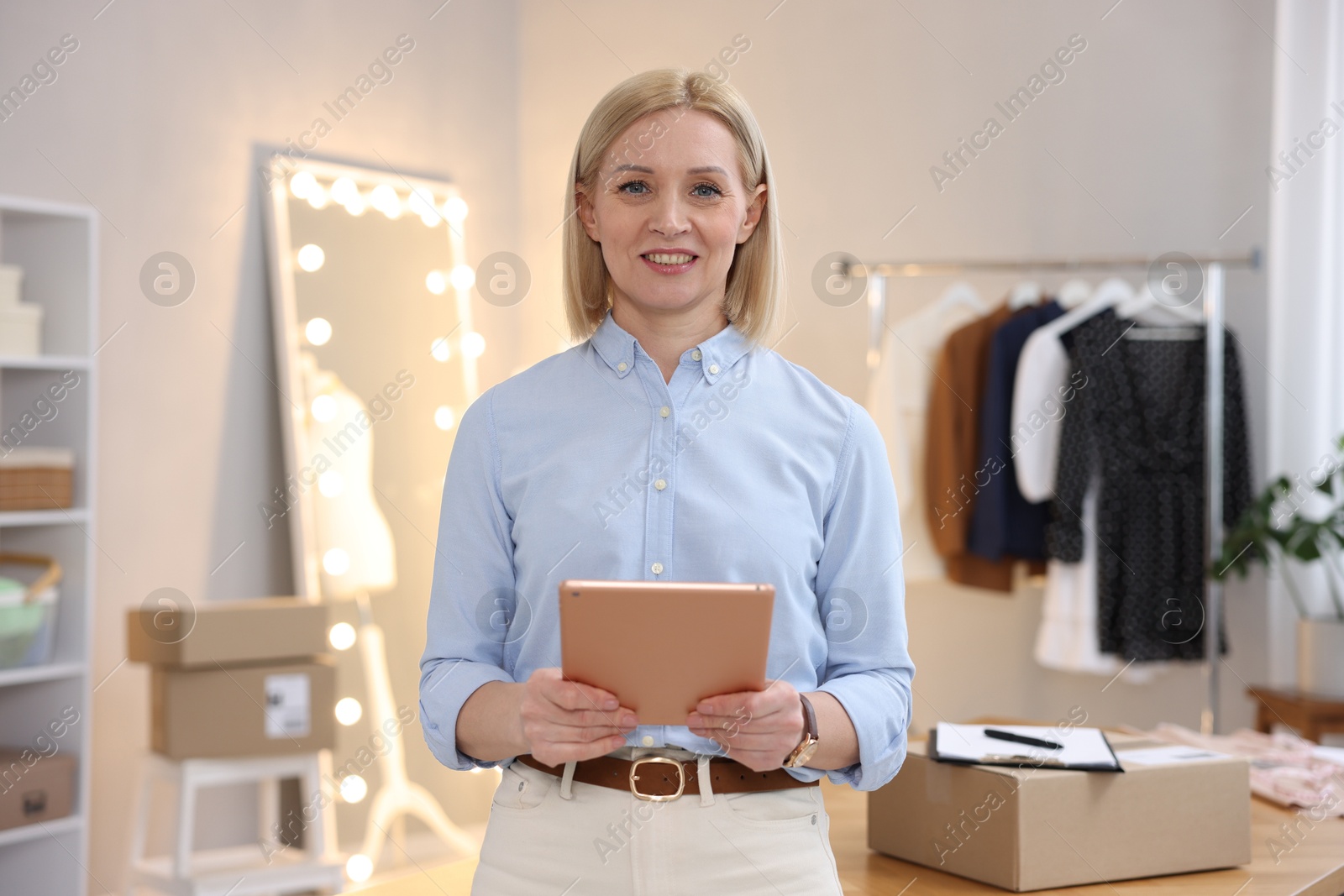 Photo of Business owner using tablet near table with parcel in her tailor shop