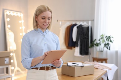 Business owner using tablet near table with parcel in her tailor shop, space for text