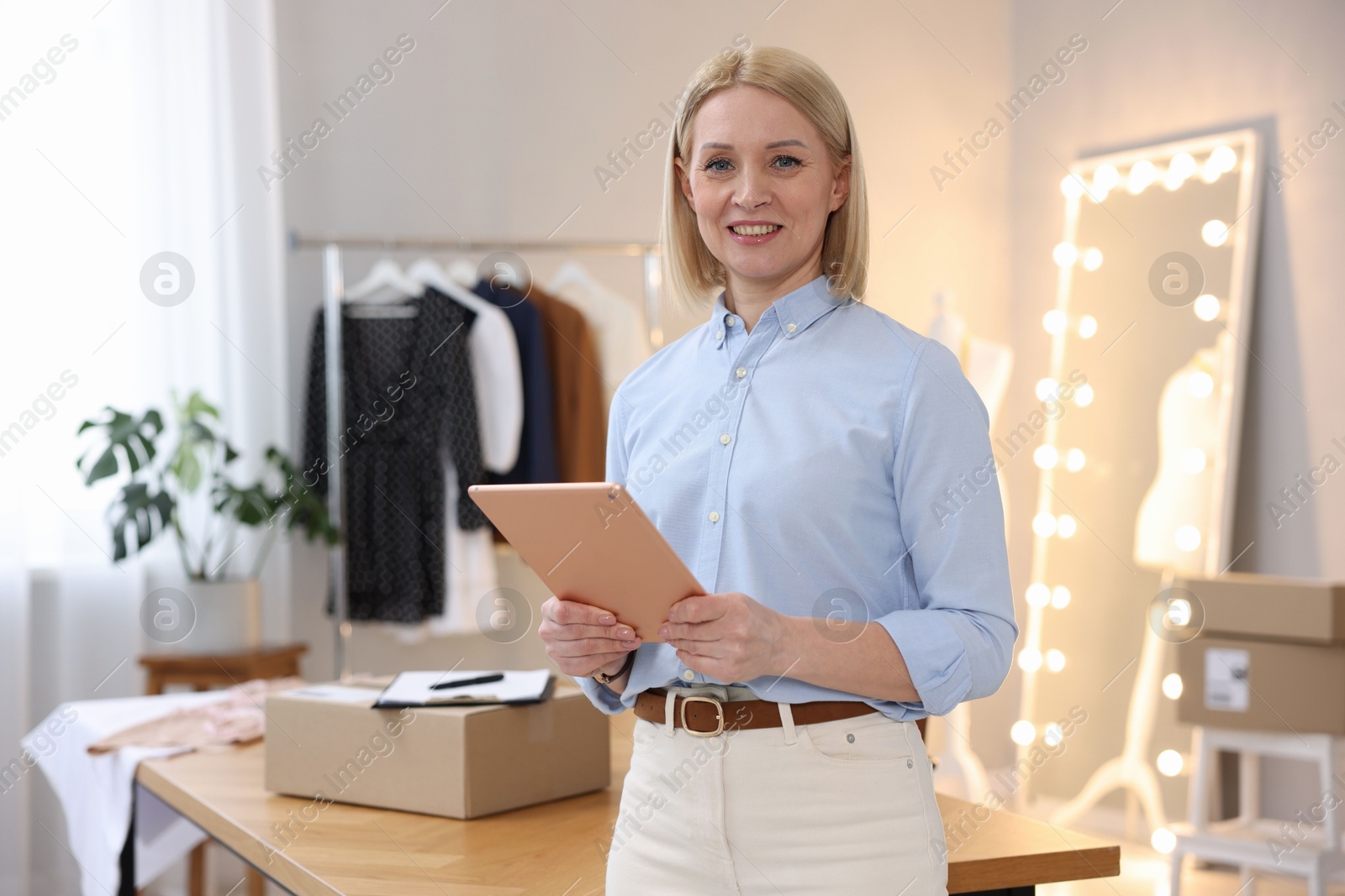 Photo of Business owner using tablet near table with parcel in her tailor shop, space for text