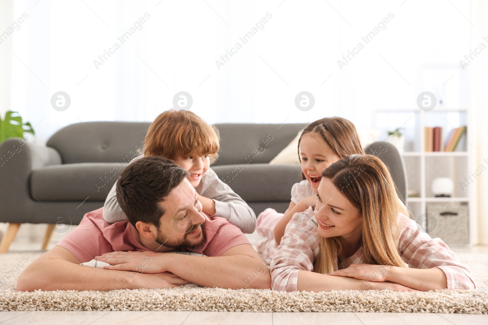 Photo of Family portrait of happy parents and their children wearing stylish pajamas on floor at home