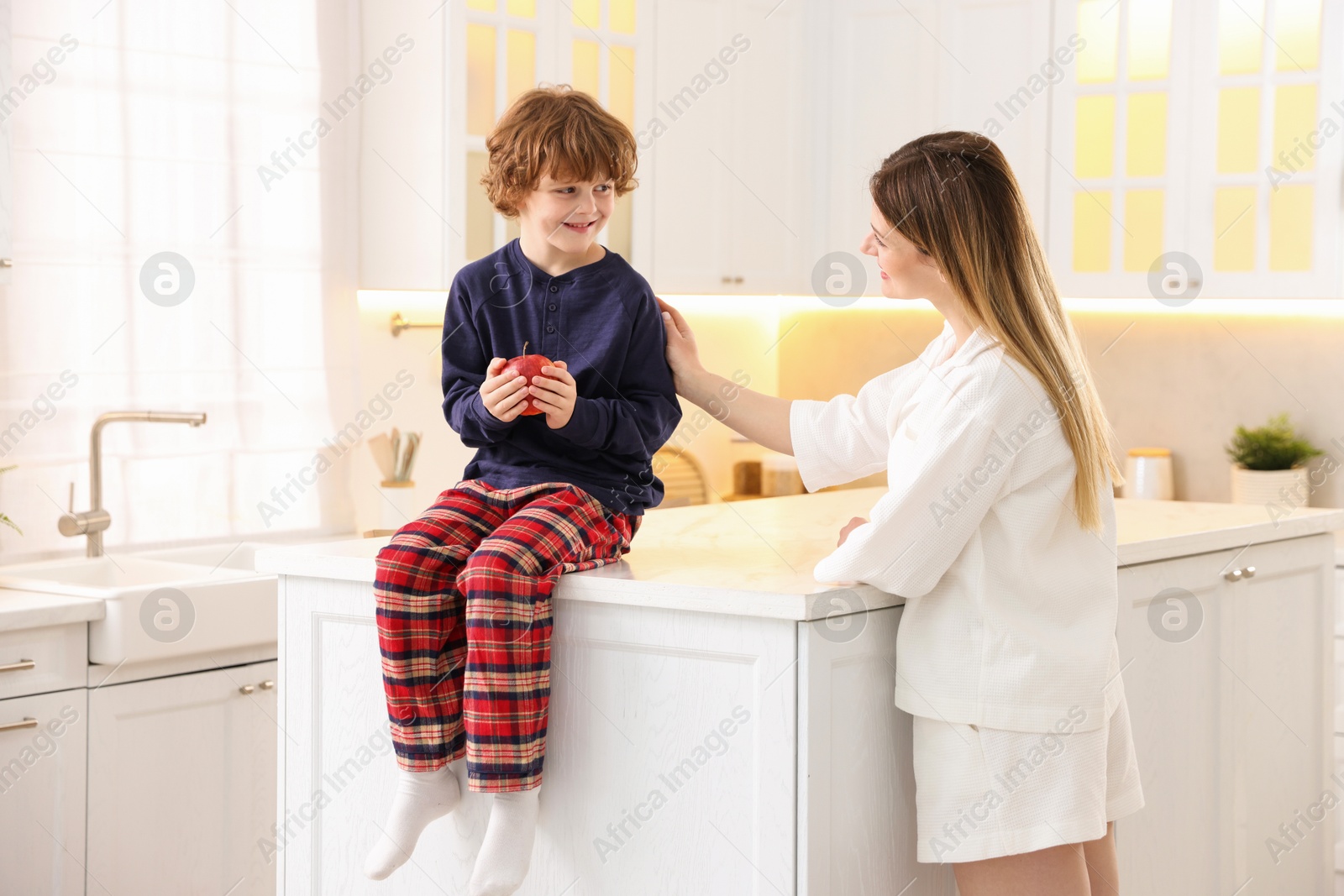 Photo of Woman and her son wearing stylish pajamas spending time together in kitchen