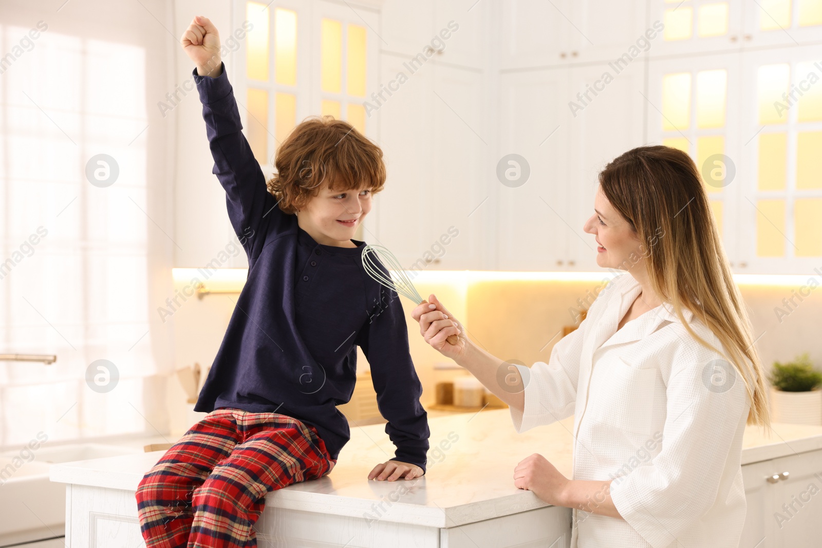 Photo of Woman and her son wearing stylish pajamas having fun in kitchen