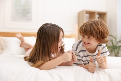 Happy children wearing pajamas showing thumbs up on bed at home