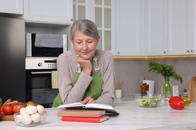 Photo of Happy woman with recipe book at table in kitchen