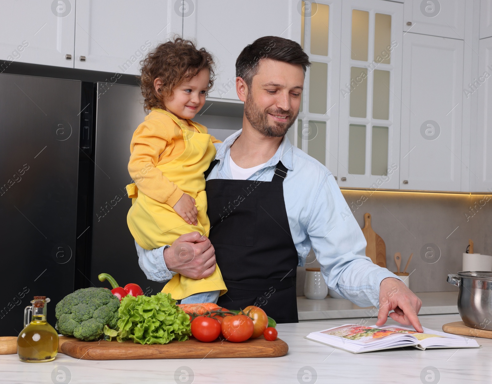 Photo of Cute little girl and her father with recipe book cooking in kitchen