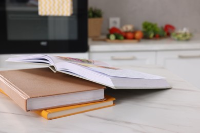 Photo of Recipe books on white marble table in kitchen, closeup. Space for text