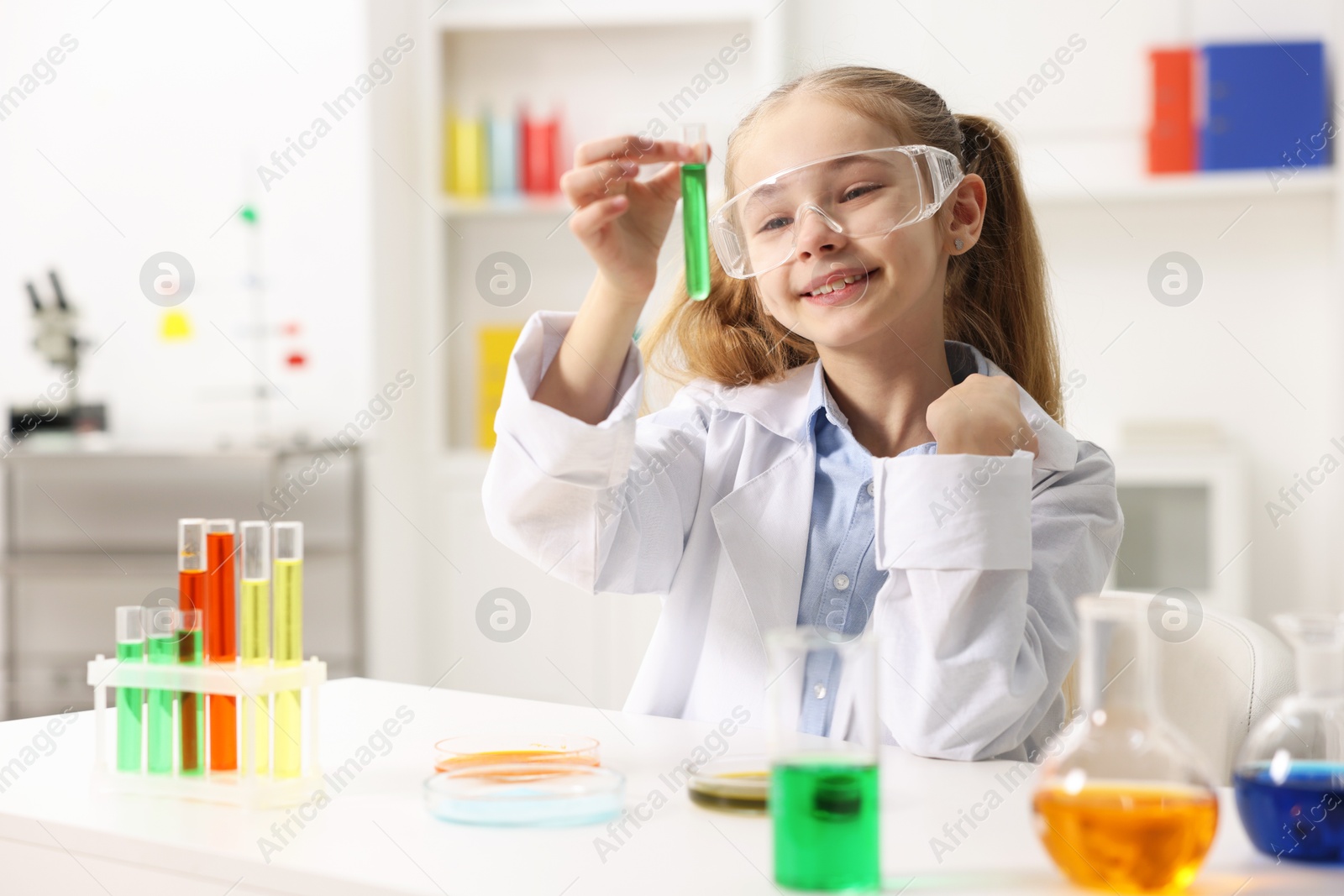 Photo of Little girl doing chemical experiment at desk indoors