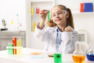 Little girl doing chemical experiment at desk indoors