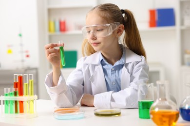 Photo of Little girl doing chemical experiment at desk indoors