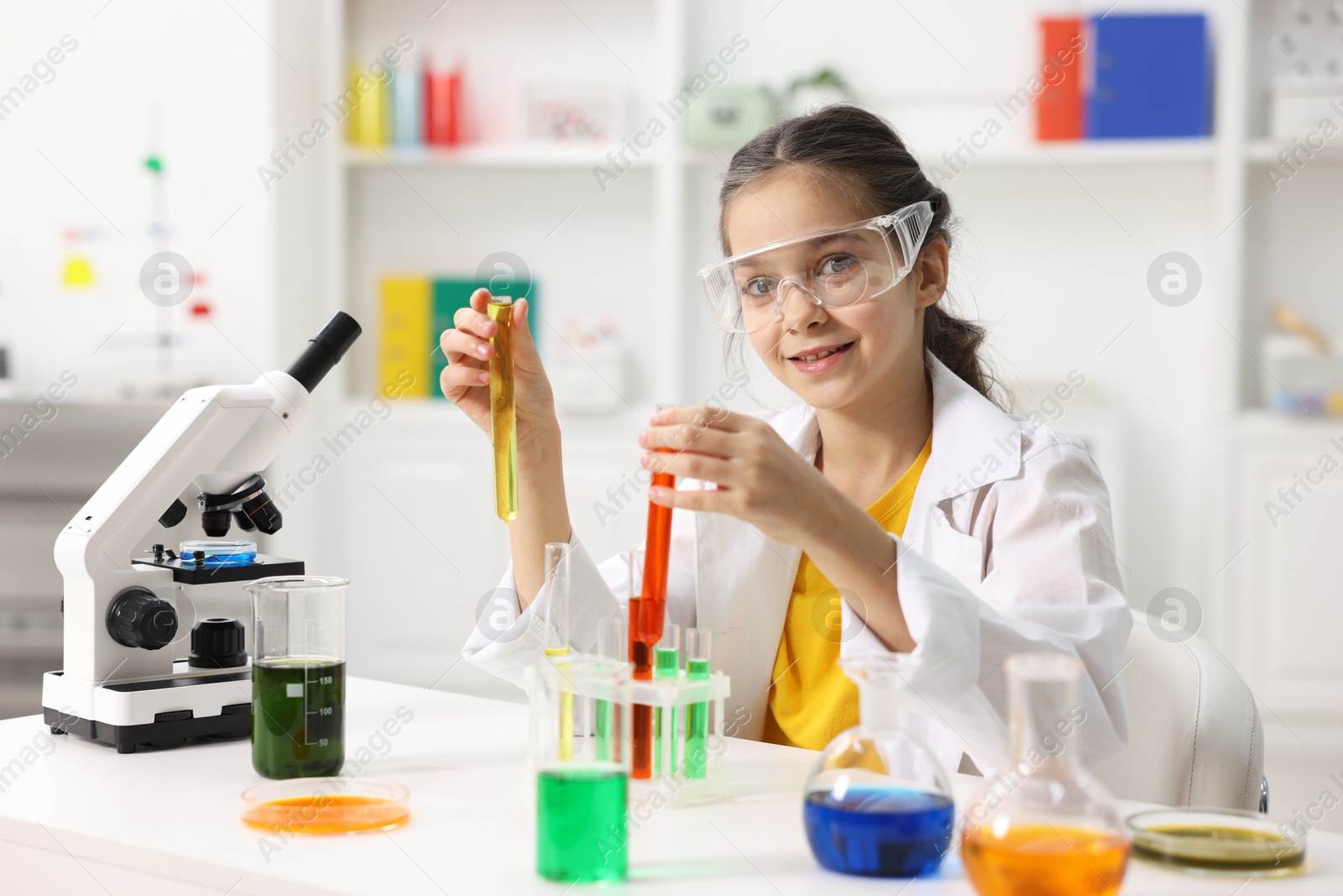 Photo of Little girl doing chemical experiment at desk indoors