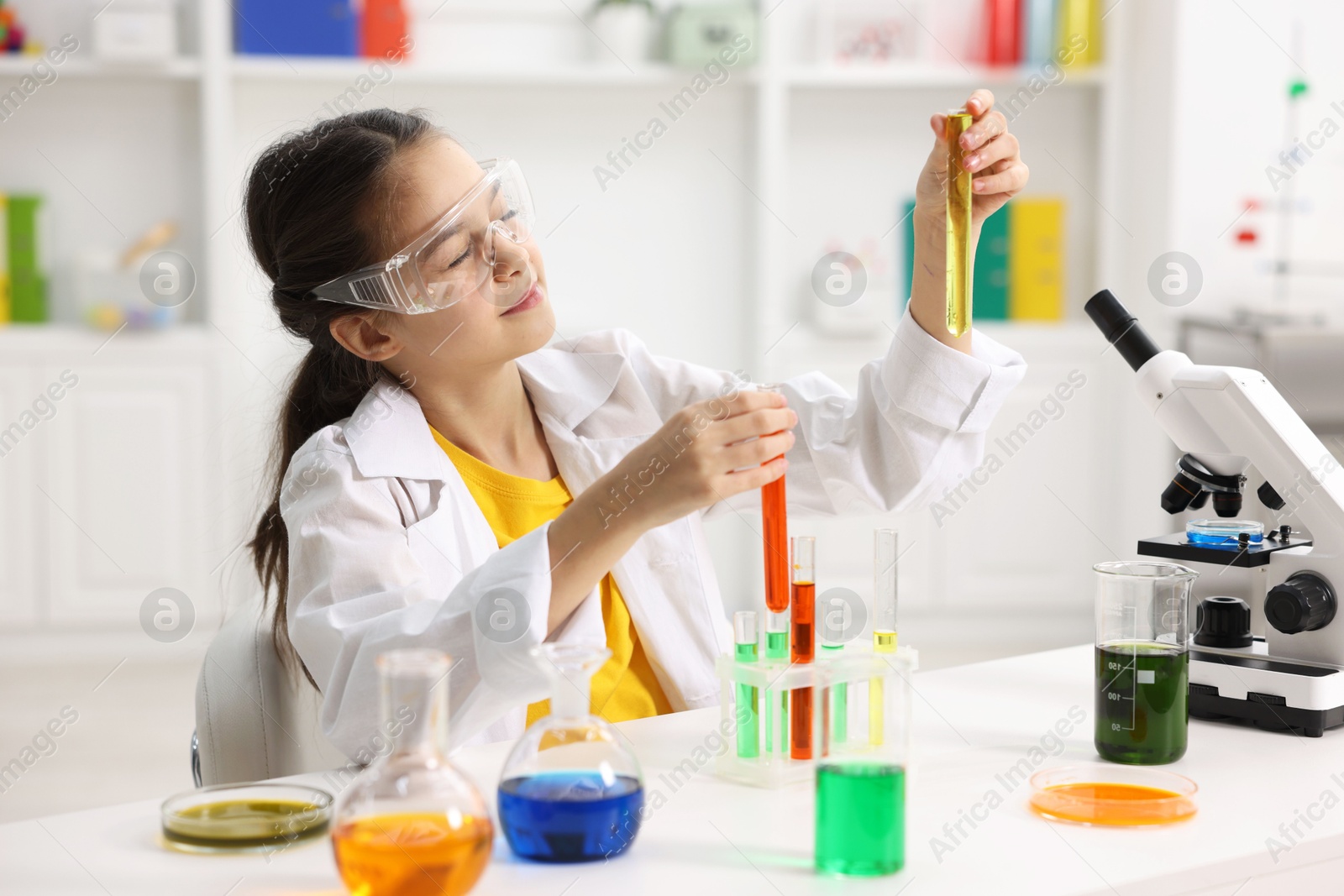 Photo of Little girl doing chemical experiment at desk indoors