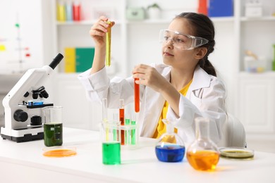 Photo of Little girl doing chemical experiment at desk indoors