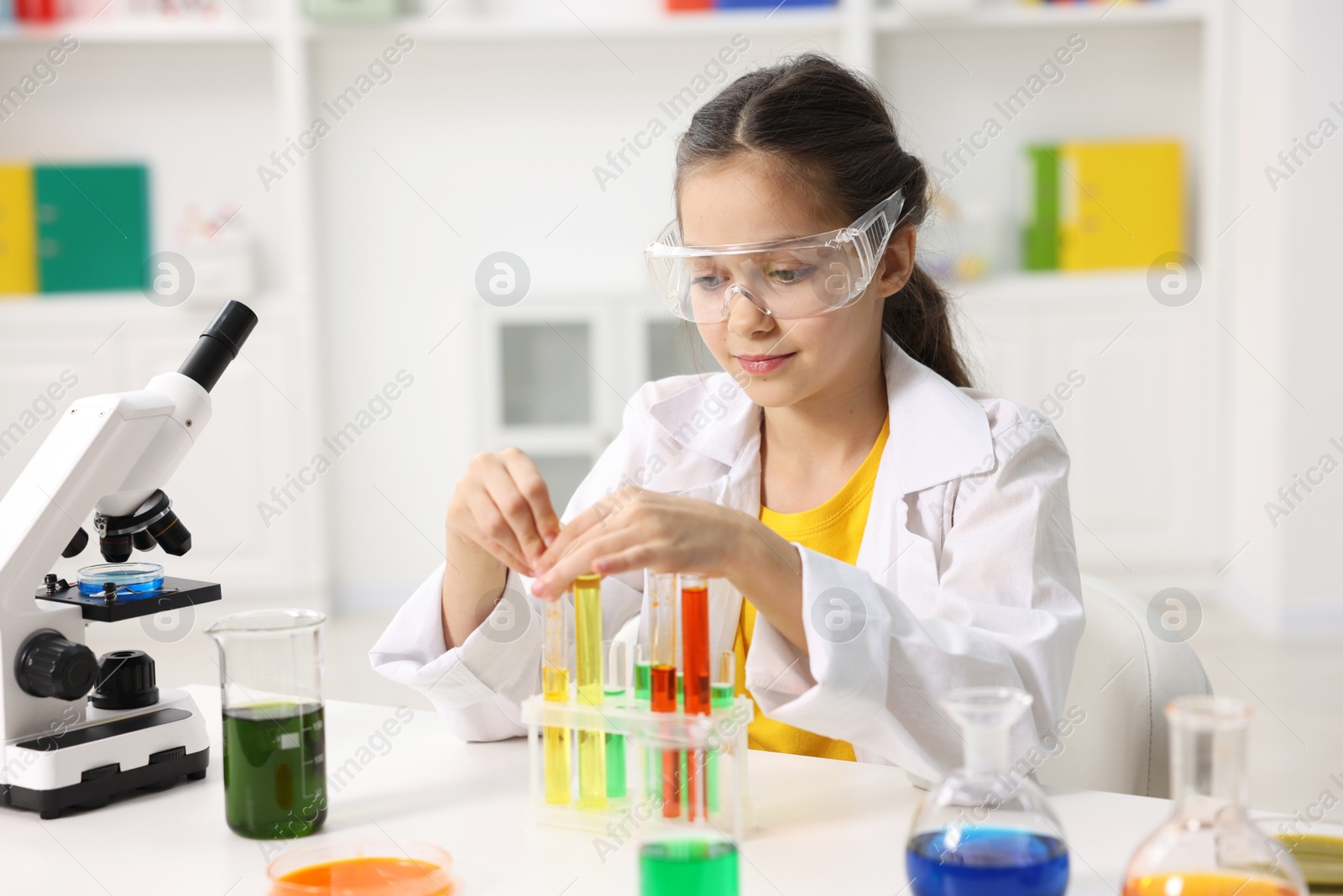 Photo of Little girl doing chemical experiment at desk indoors