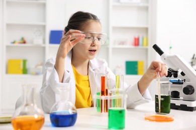 Little girl doing chemical experiment at desk indoors