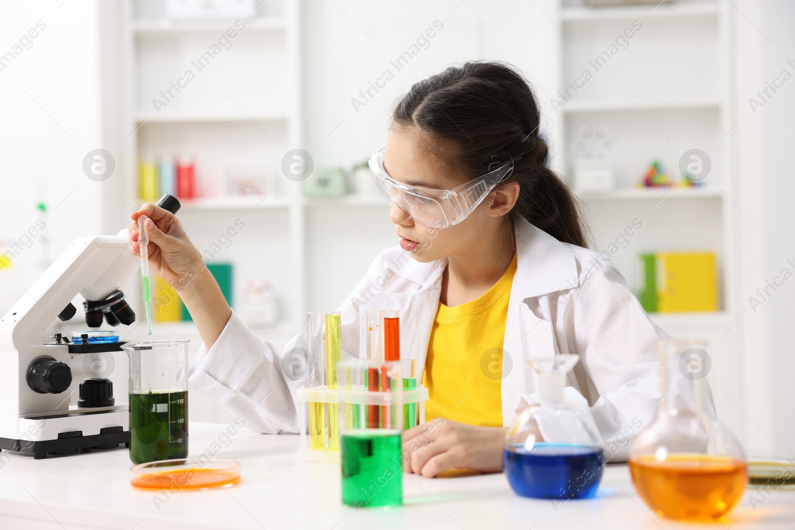 Photo of Little girl doing chemical experiment at desk indoors