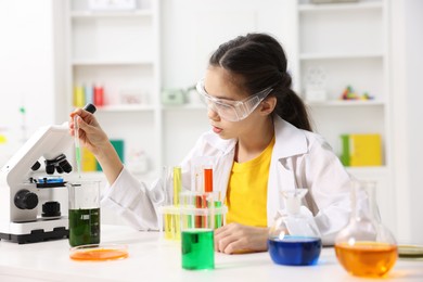 Little girl doing chemical experiment at desk indoors