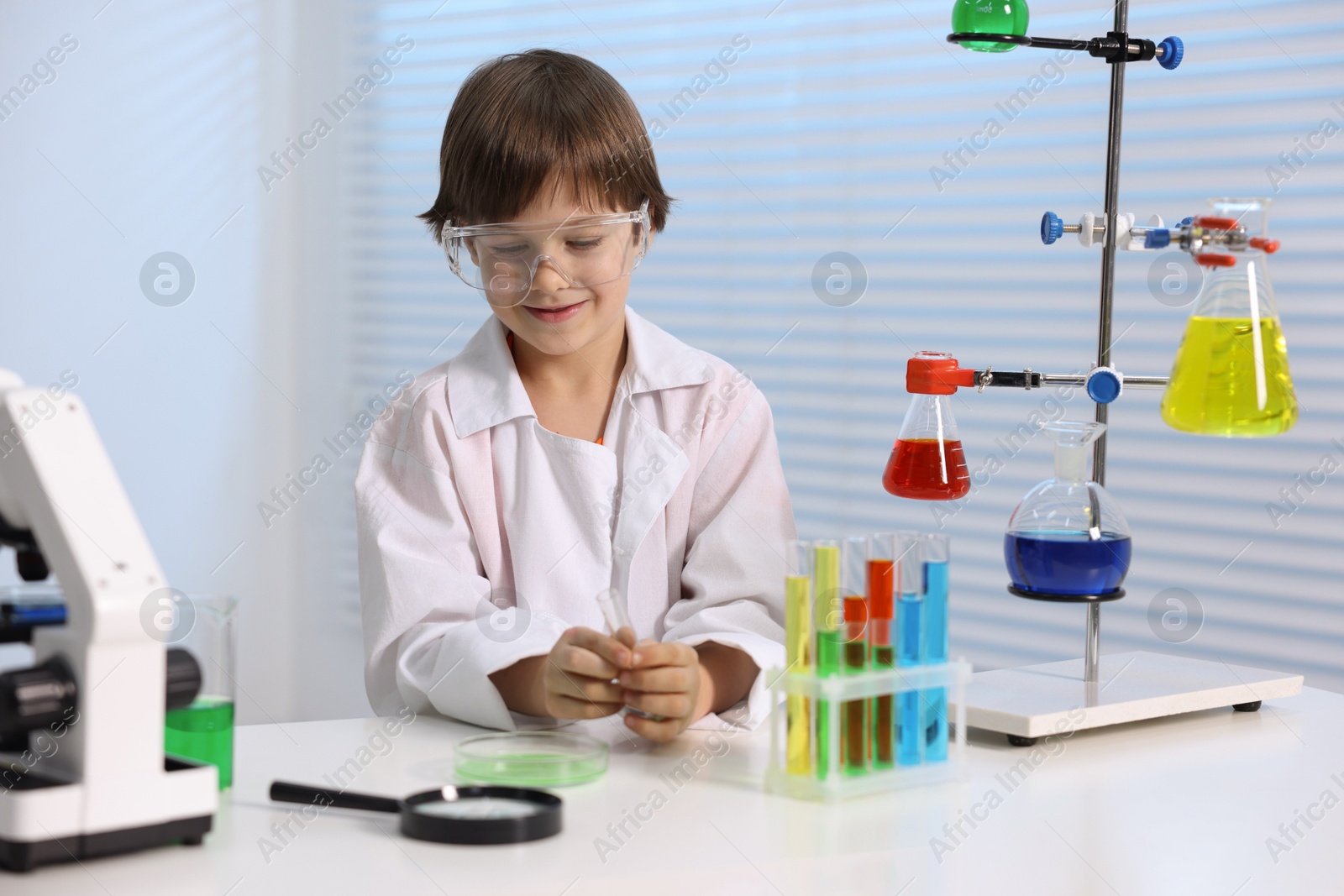 Photo of Little boy doing chemical experiment at desk indoors