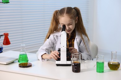 Photo of Little girl working with microscope at desk indoors