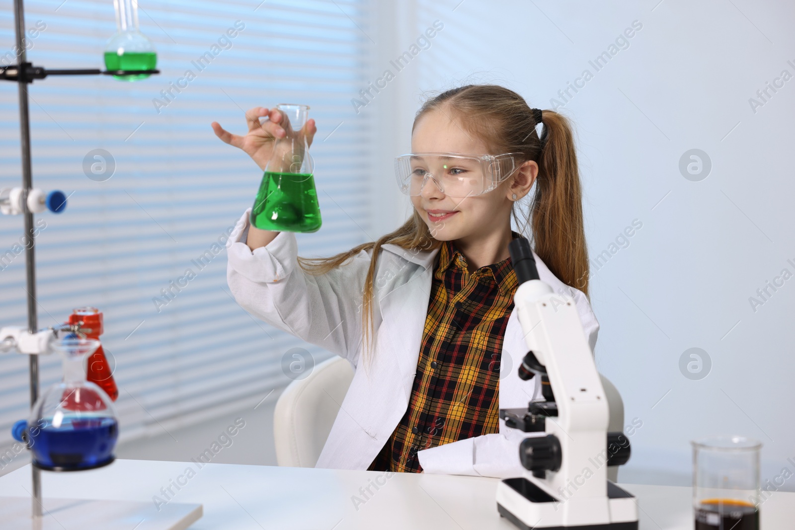 Photo of Little girl doing chemical experiment at desk indoors