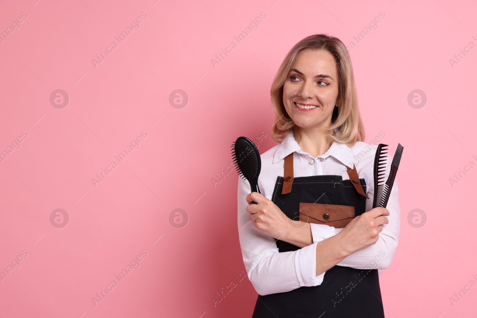 Photo of Smiling hairdresser with combs and brush on pink background, space for text