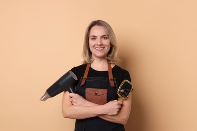 Smiling hairdresser with dryer and brush on beige background