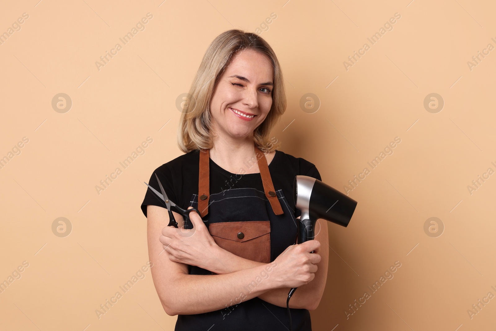 Photo of Smiling hairdresser with dryer and scissors on beige background