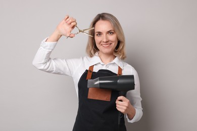 Smiling hairdresser with dryer and scissors on gray background