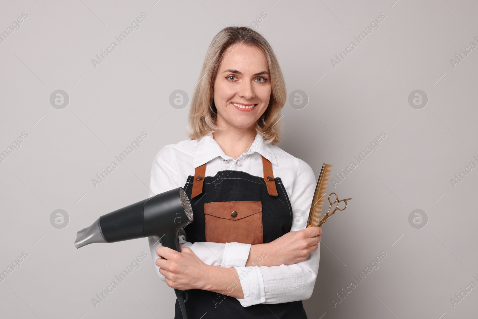 Photo of Smiling hairdresser with dryer, scissors and comb on gray background