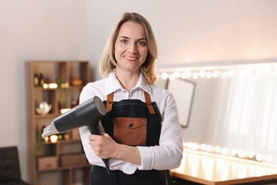 Smiling hairdresser with dryer in beauty salon