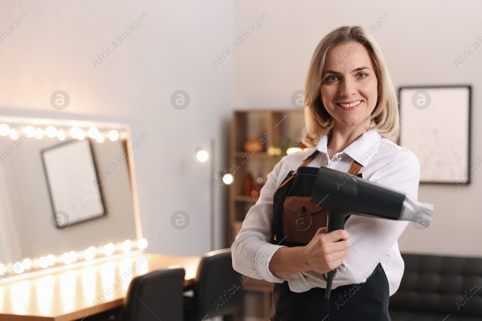 Photo of Smiling hairdresser with dryer in beauty salon, space for text