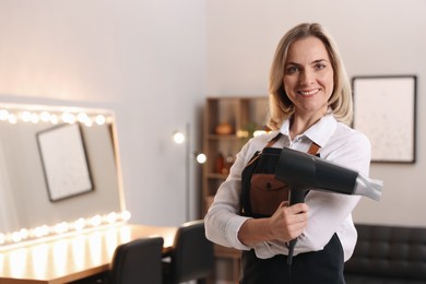 Smiling hairdresser with dryer in beauty salon, space for text