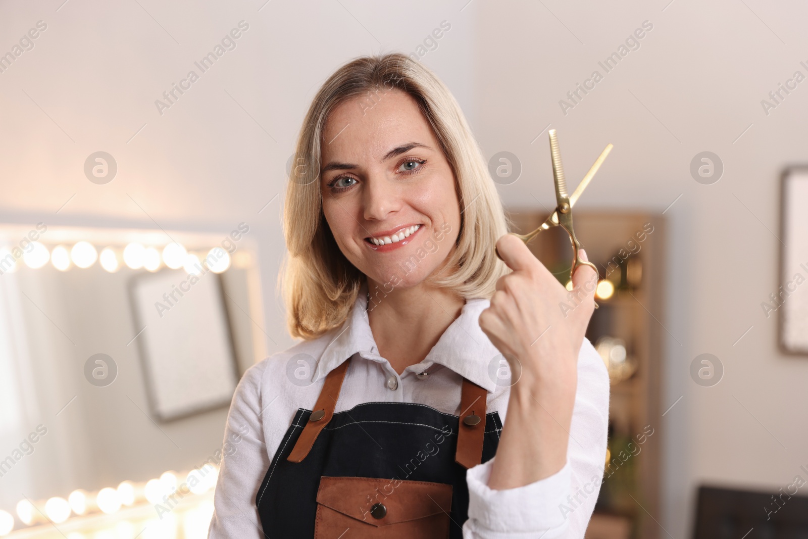 Photo of Smiling hairdresser with scissors in beauty salon