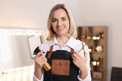 Photo of Smiling hairdresser with scissors and spray bottle in beauty salon