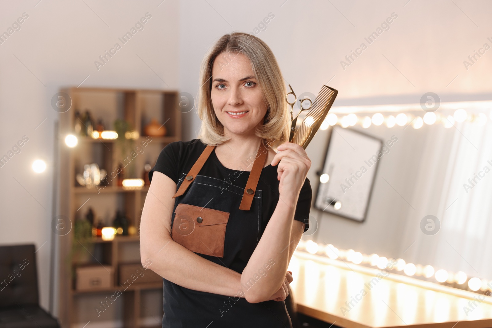 Photo of Smiling hairdresser with scissors and comb in beauty salon