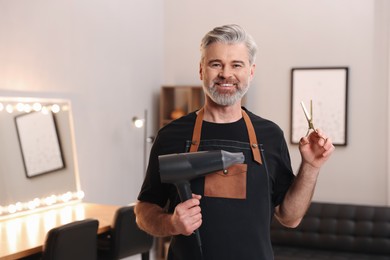 Photo of Smiling hairdresser with dryer and scissors in beauty salon