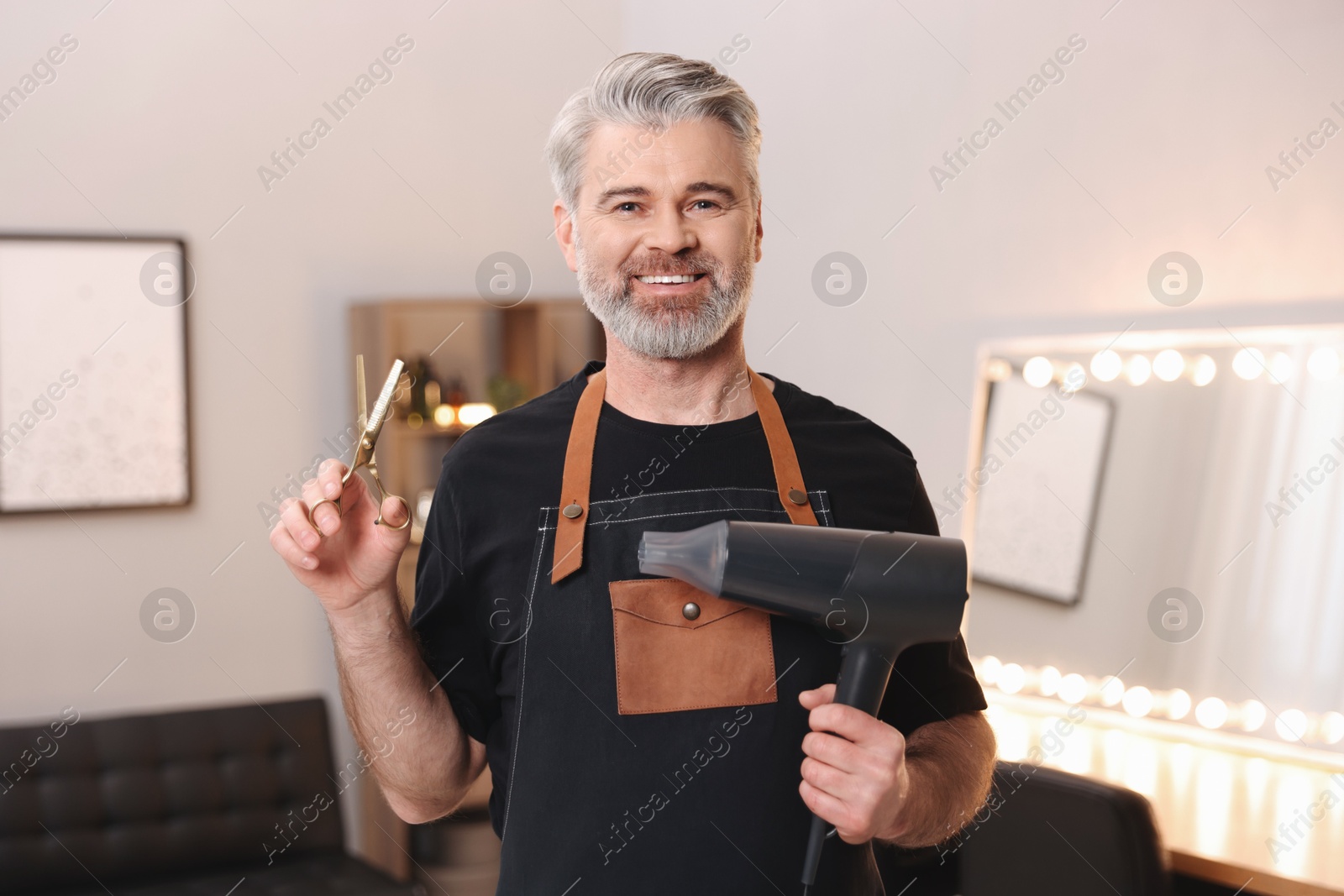 Photo of Smiling hairdresser with dryer and scissors in beauty salon