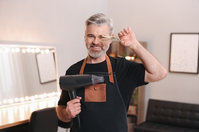 Photo of Smiling hairdresser with dryer and scissors in beauty salon