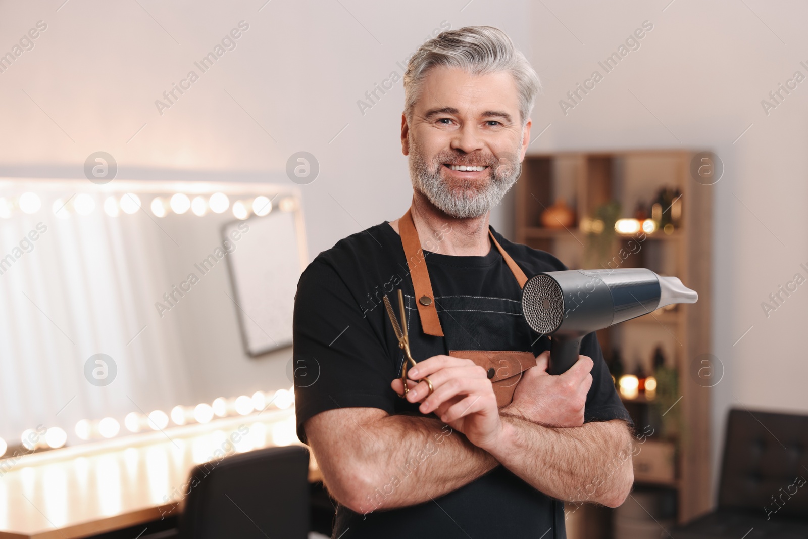 Photo of Smiling hairdresser with dryer and scissors in beauty salon