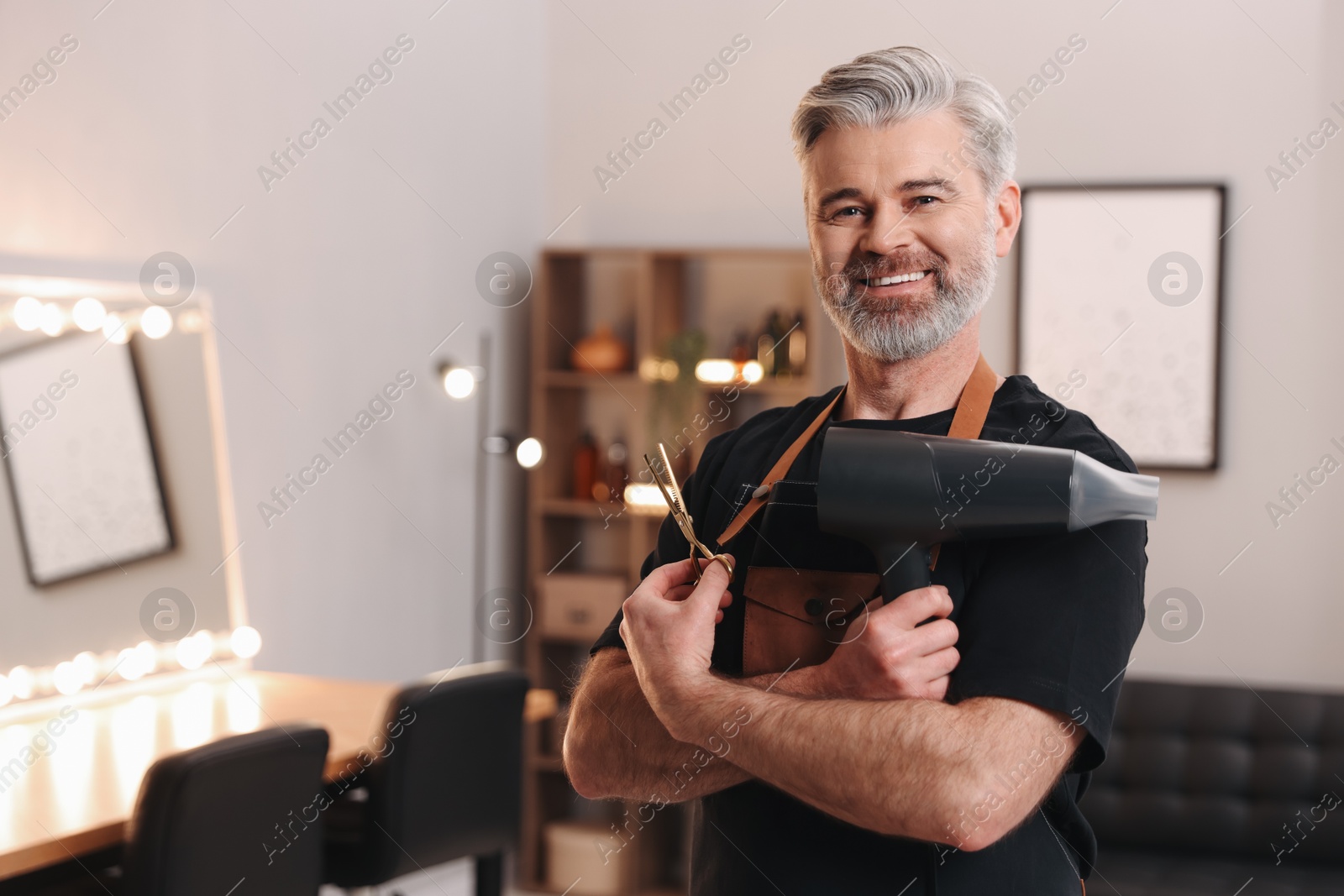 Photo of Smiling hairdresser with dryer and scissors in beauty salon