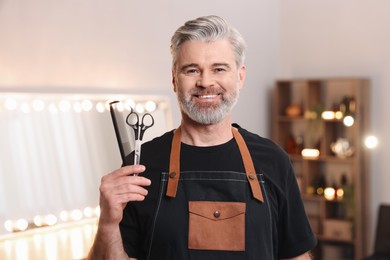 Photo of Smiling hairdresser with comb and scissors in beauty salon