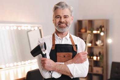 Photo of Smiling hairdresser with dryer and comb in beauty salon